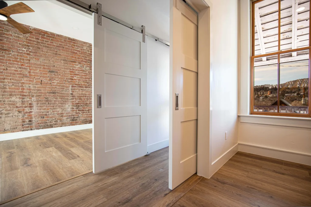 Modern interior by Durango Remodeling in Colorado featuring sliding barn doors, exposed brick accent wall, wood flooring, and window with mountain views.