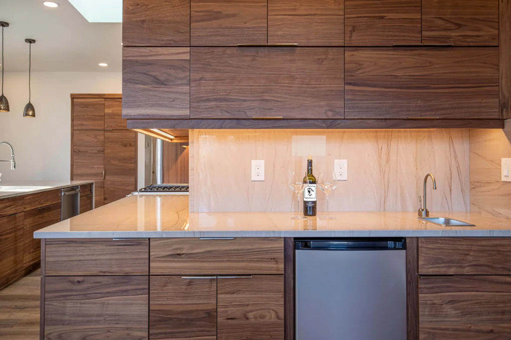 Modern kitchen by Durango Remodeling in Colorado with flat-panel wood cabinetry, stone countertops, built-in beverage fridge, under-cabinet lighting, and prep sink.