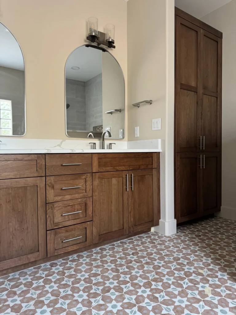 Custom bathroom by Durango Remodeling in Colorado with wood vanity, quartz countertop, arched mirror, patterned tile flooring, and built-in storage cabinetry.